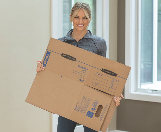 Woman carrying an unassembled box smiling at the camera