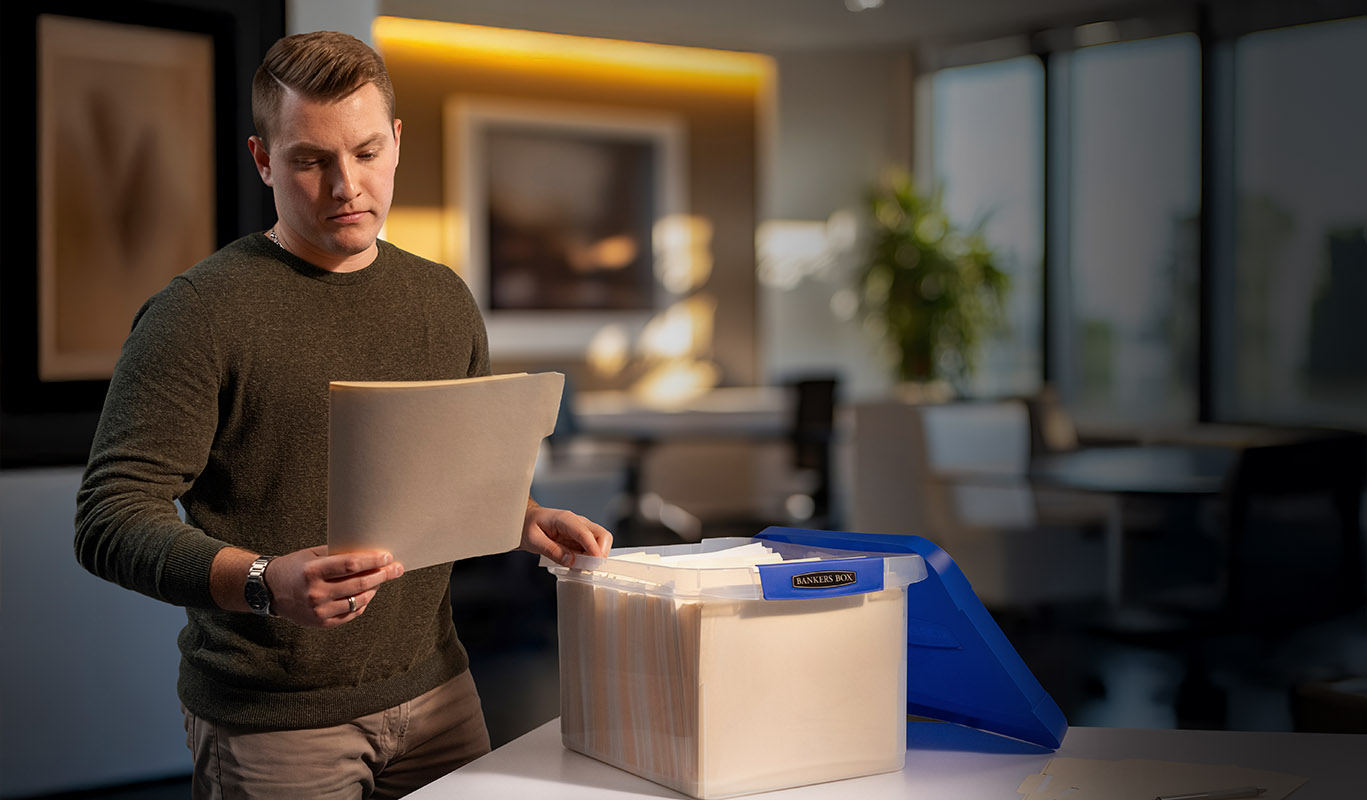 Man looking at a file folder he just took out of a plastic storage box