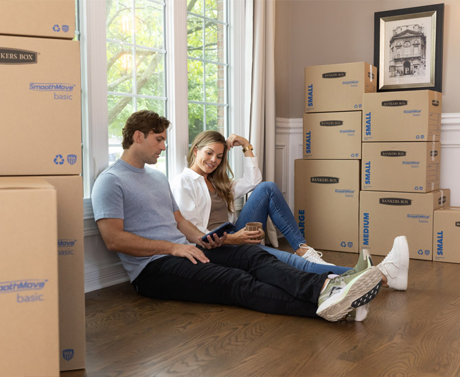 Man and woman sitting on floor next to stacked boxes