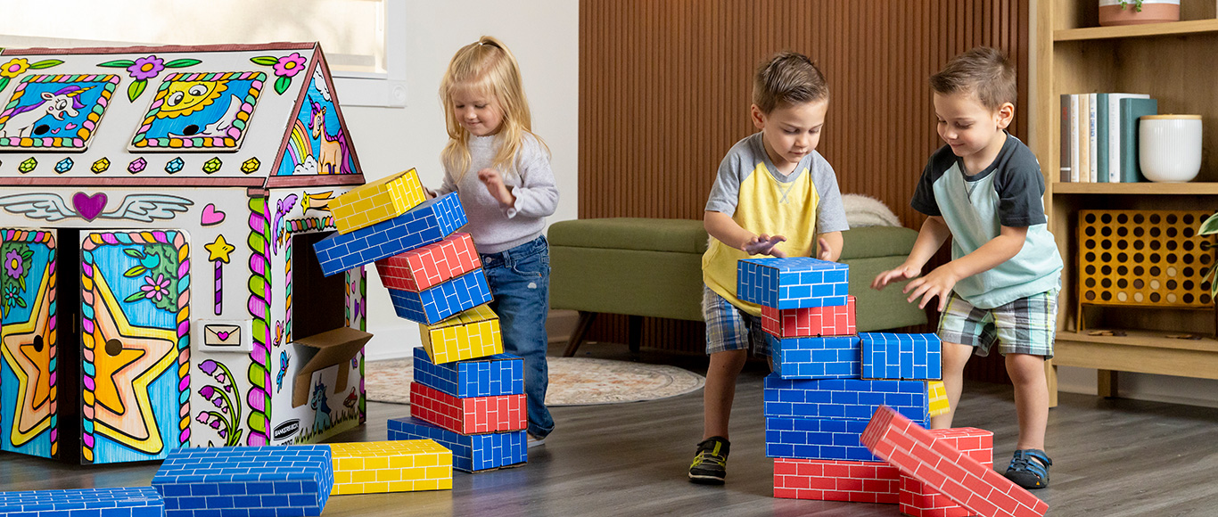 Image of a two boys and a girl playing in and around an At Play Cardboard Playhouse