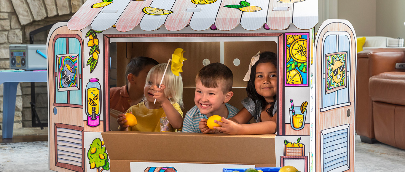 Image of a two boys and two girls playing in and around an At Play Cardboard Playhouse