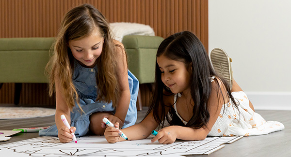 two small girls coloring on the side of a cardboard playhouse