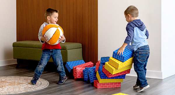 two small boys playing with cardboard blocks and a ball to knock them down
