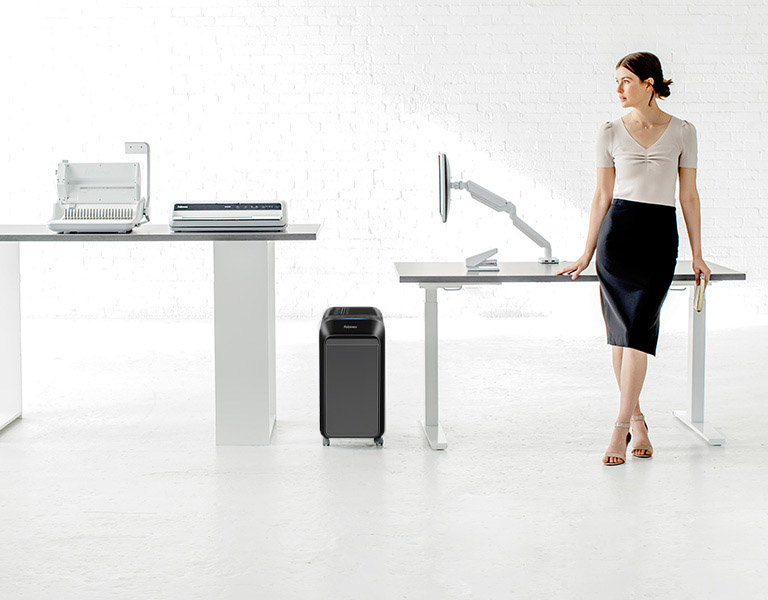 Woman sitting at desk looking off-screen while next to a shredder