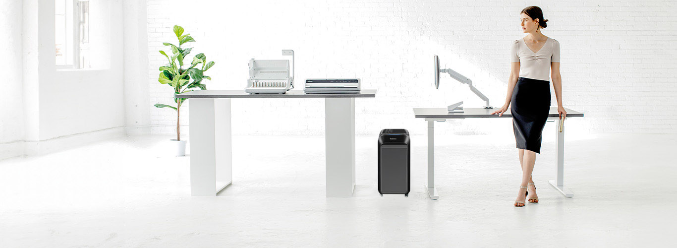 Woman sitting at desk looking off-screen while next to a shredder