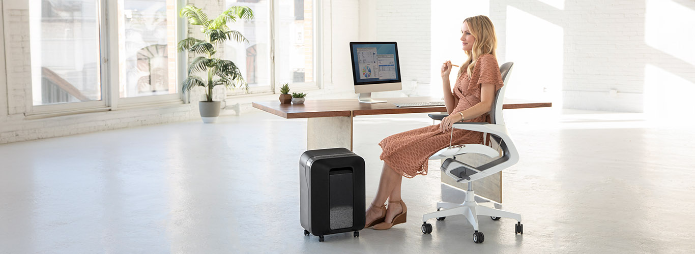 Woman sitting at desk looking off-screen while next to a shredder