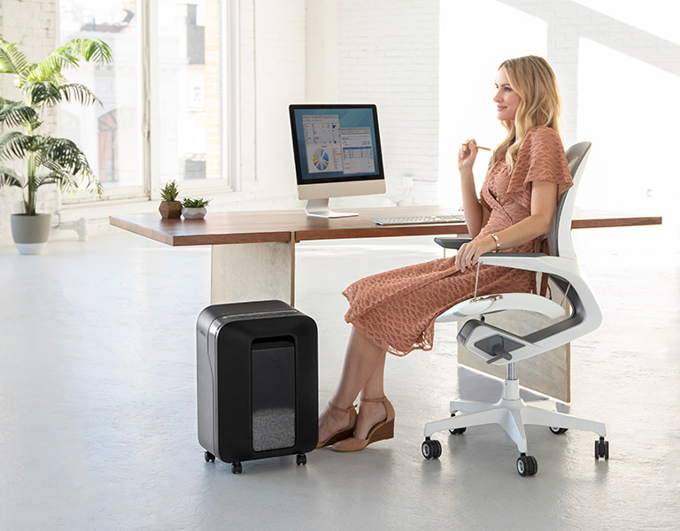 Woman sitting at desk looking off-screen while next to a shredder