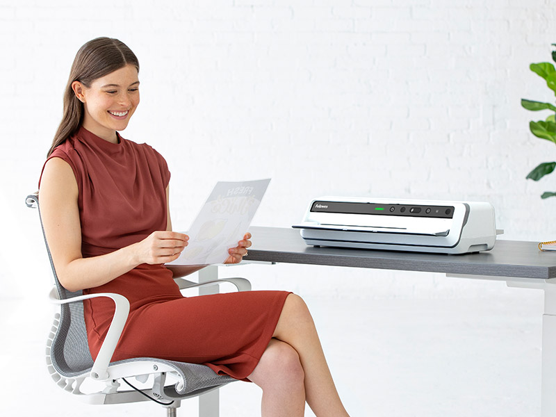 Woman sitting at desk looking off-screen while next to a shredder