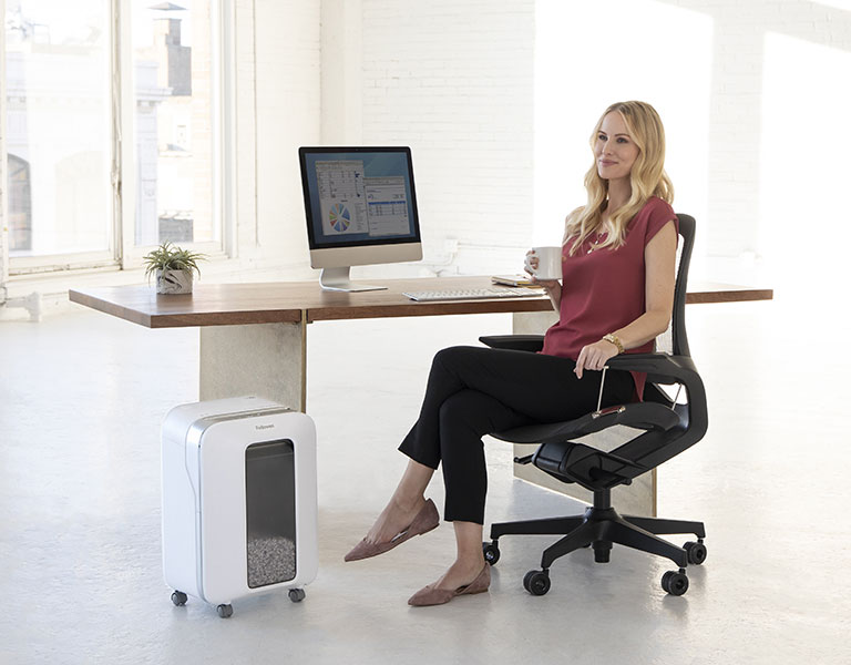 Woman sitting at desk looking off-screen while next to a shredder