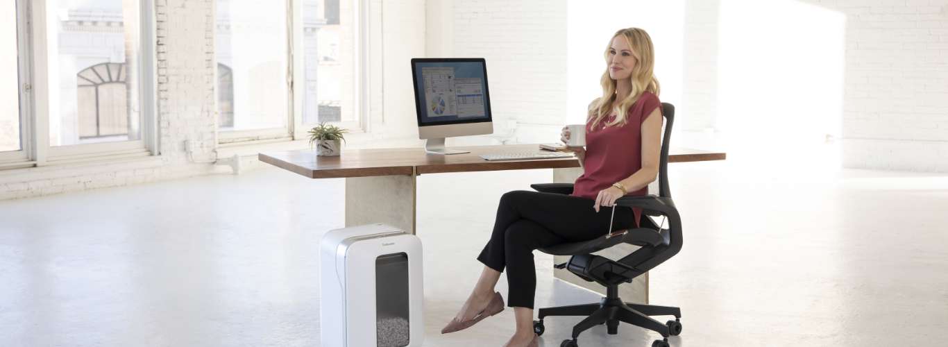 Woman sitting at desk looking off-screen while next to a shredder