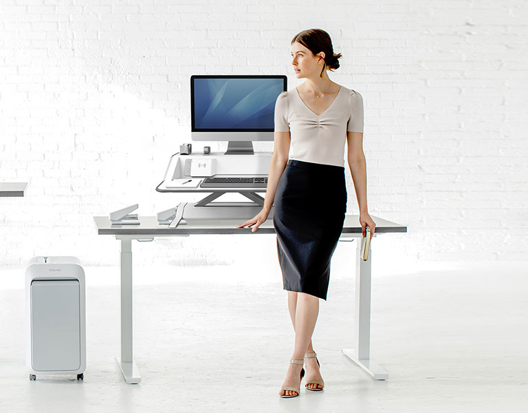 Woman sitting at desk looking off-screen while next to a shredder