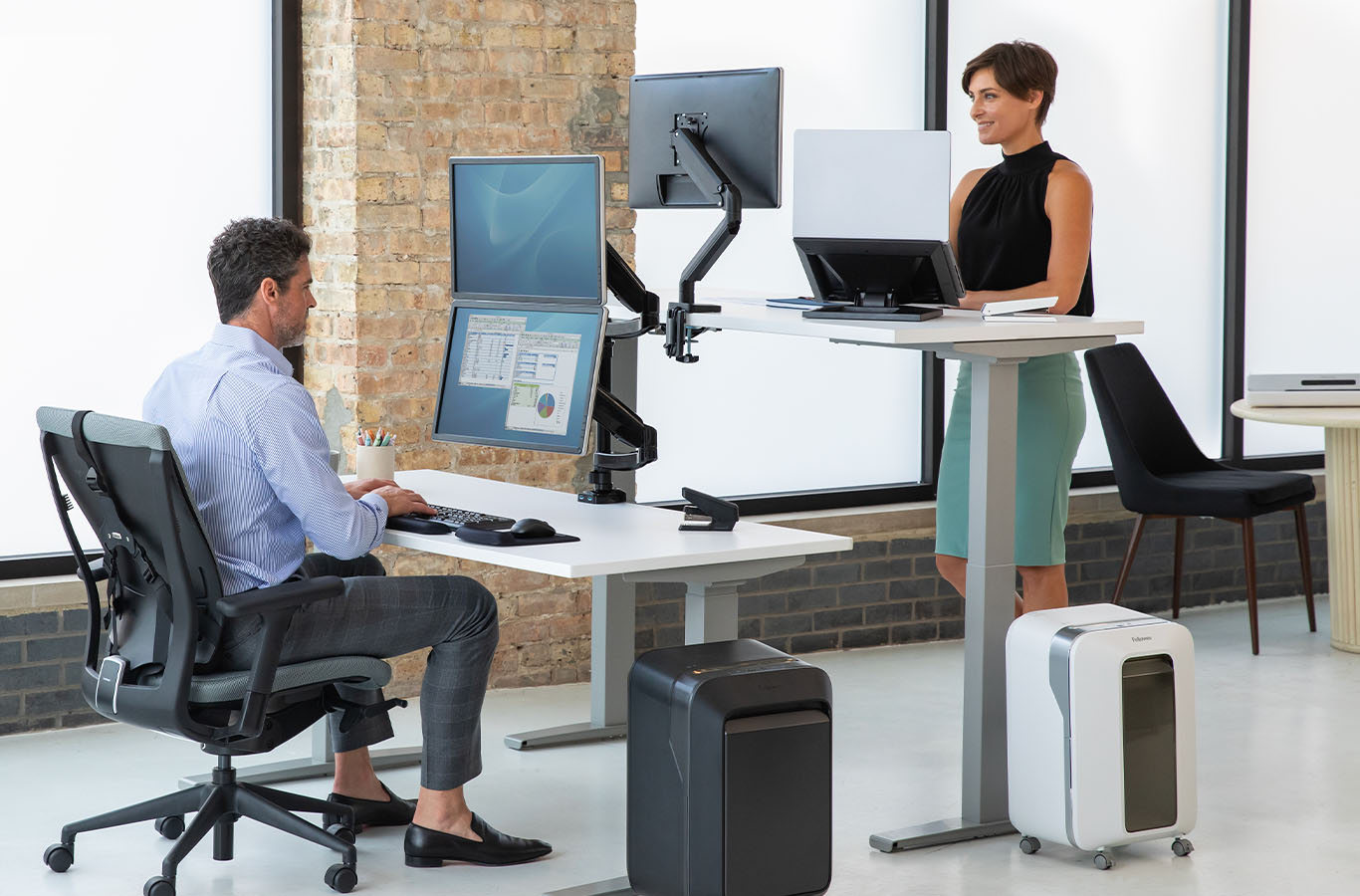 man seated at desk working, woman on the opposite side of him standing at her standing desk also working