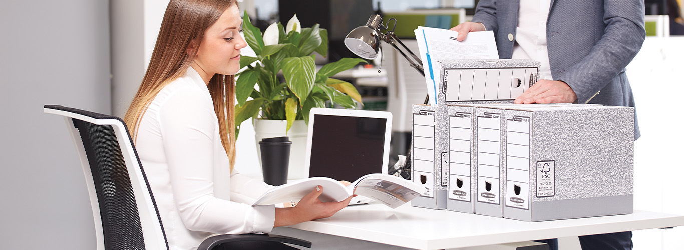 Woman sitting at desk looking off-screen while next to a shredder