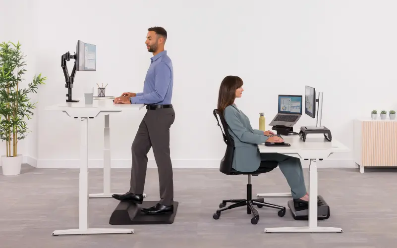 Man stood at sit-stand desk woman sat at sit-stand desk