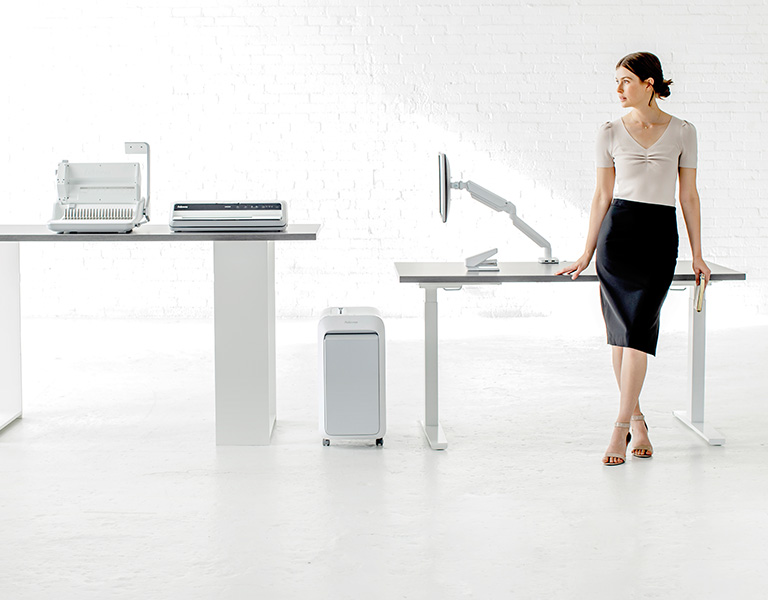 Woman sitting at desk looking off-screen while next to a shredder