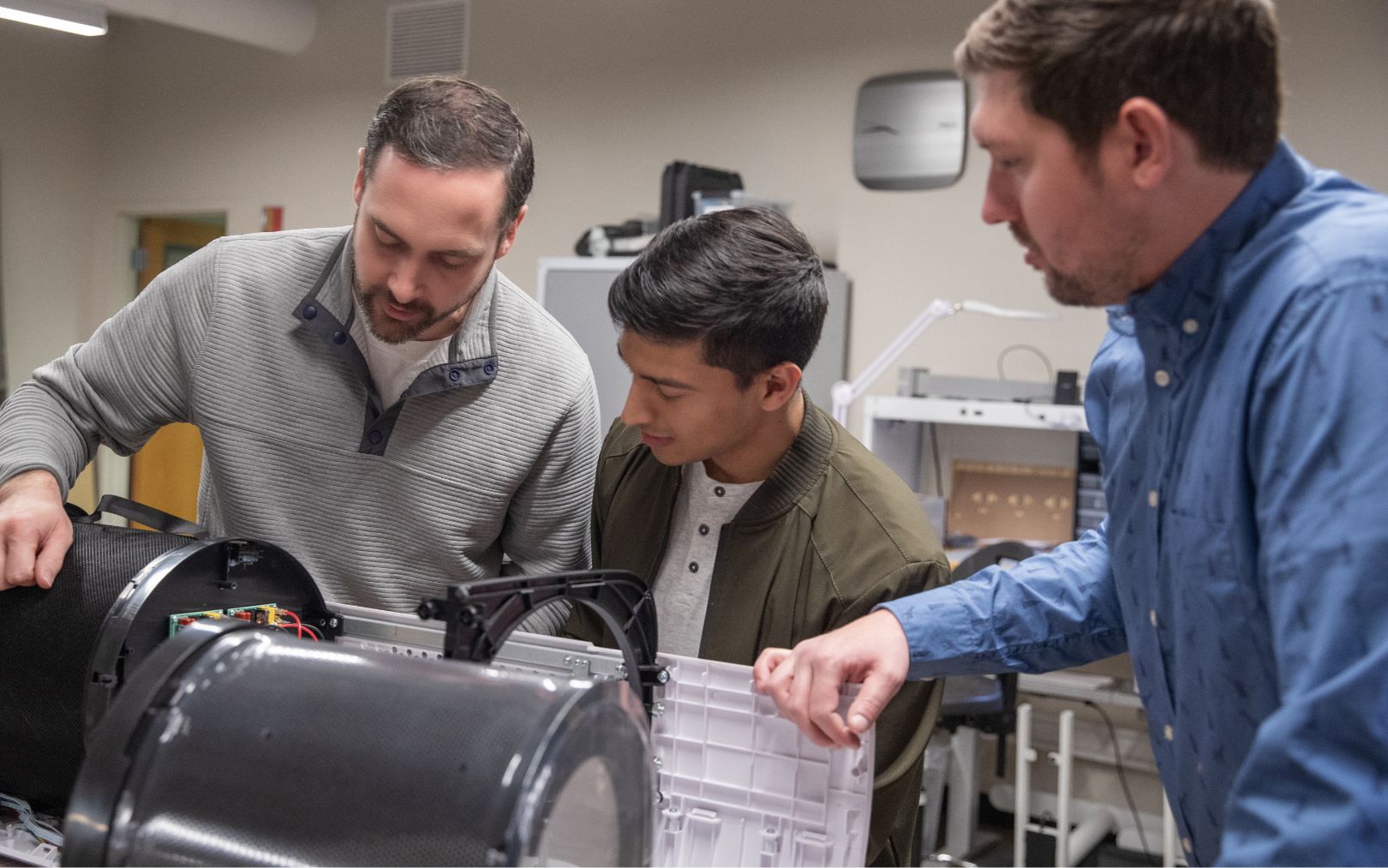 three men standing over a prototype discussing something
