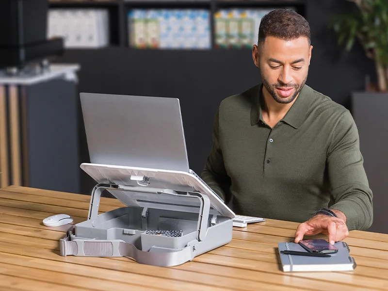 Man looking at a mobile phone beside a laptop stand