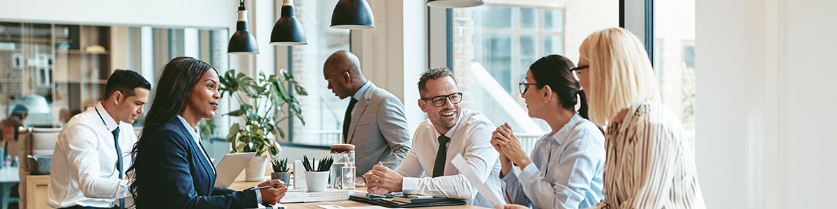 multiple people sitting around a long skinny table in an office building