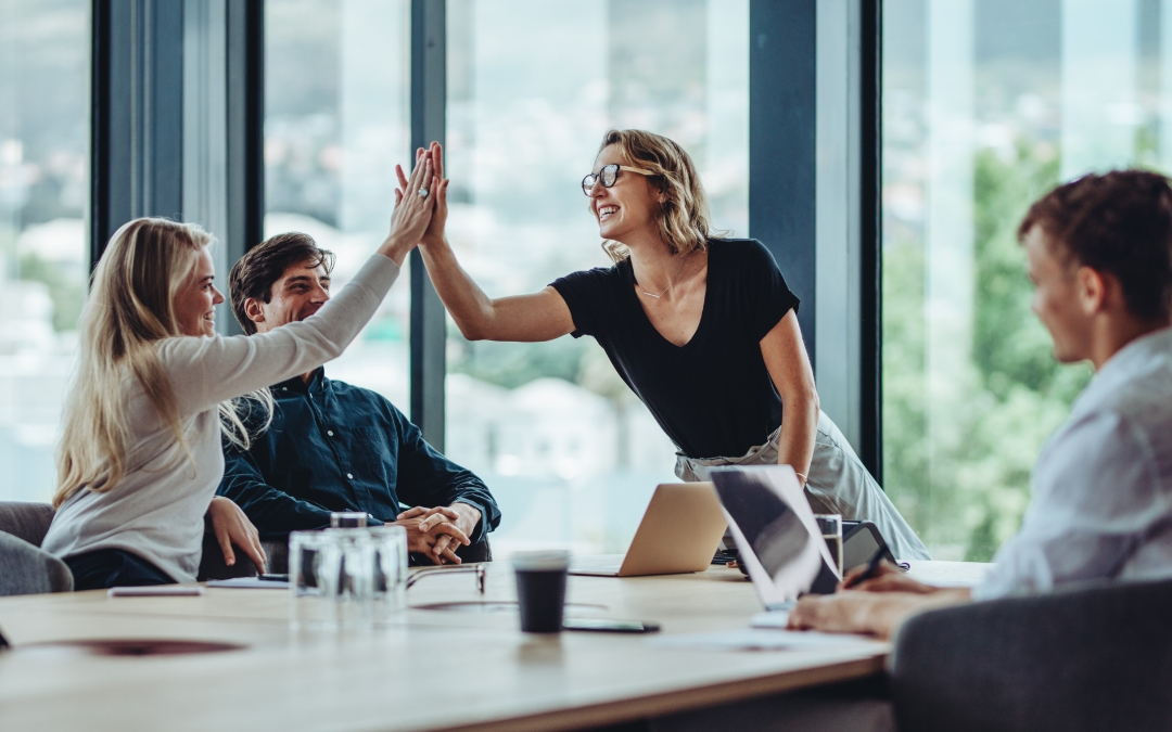 Image of people siting around a conference table, two of them are high-fiving