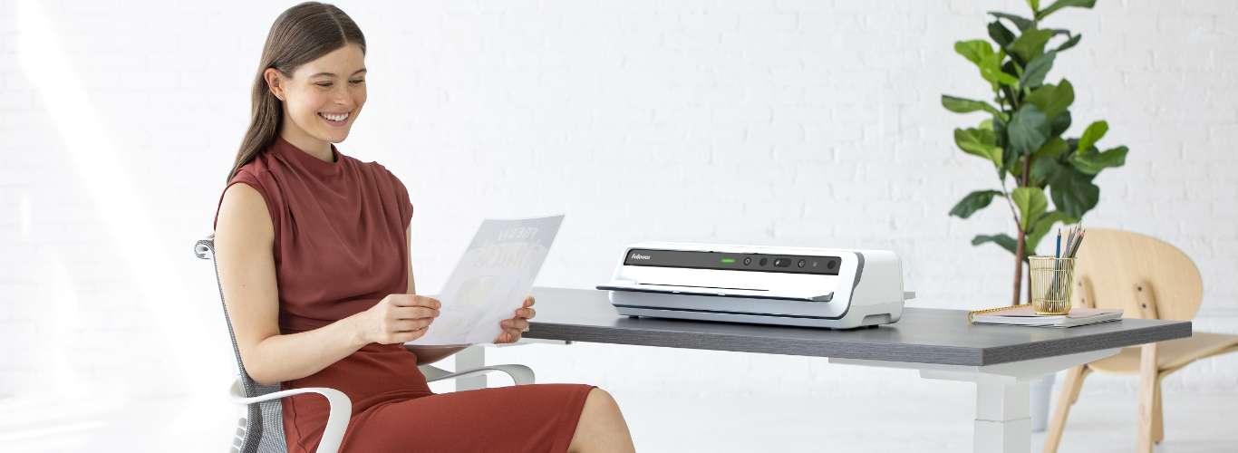 Woman sitting at desk looking off-screen while next to a shredder