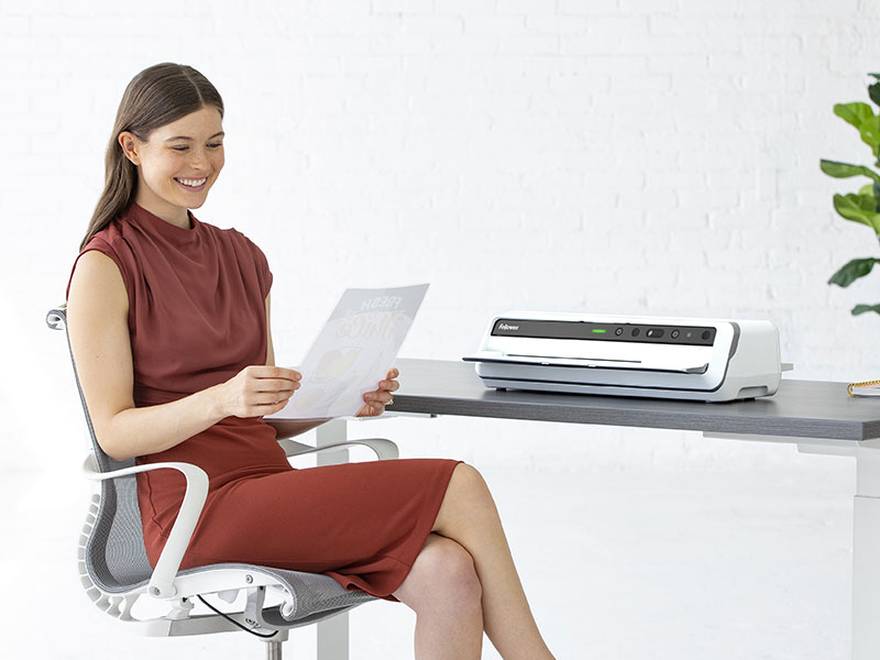 Woman sitting at desk looking off-screen while next to a shredder