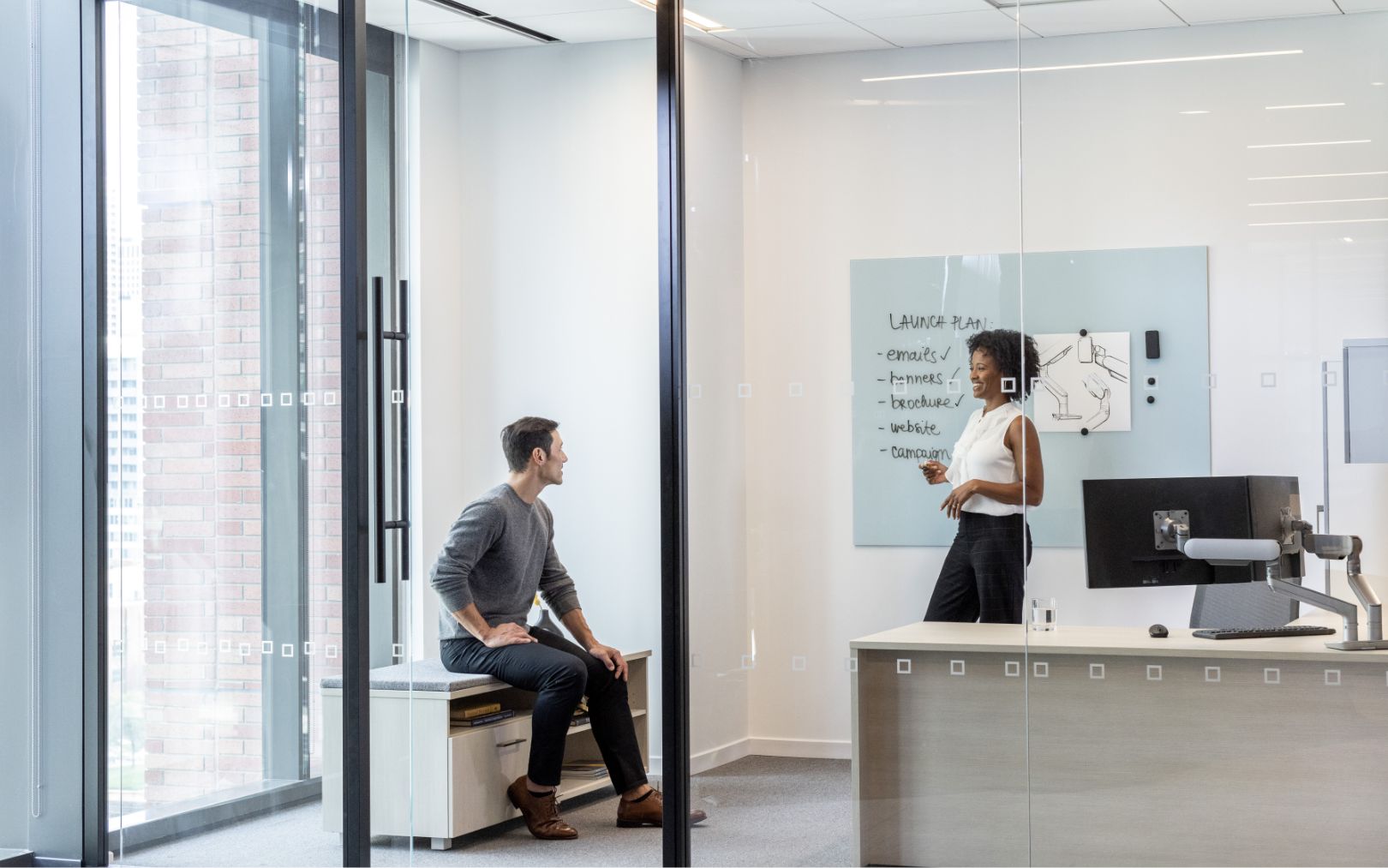 sitting man talking with standing woman in her office