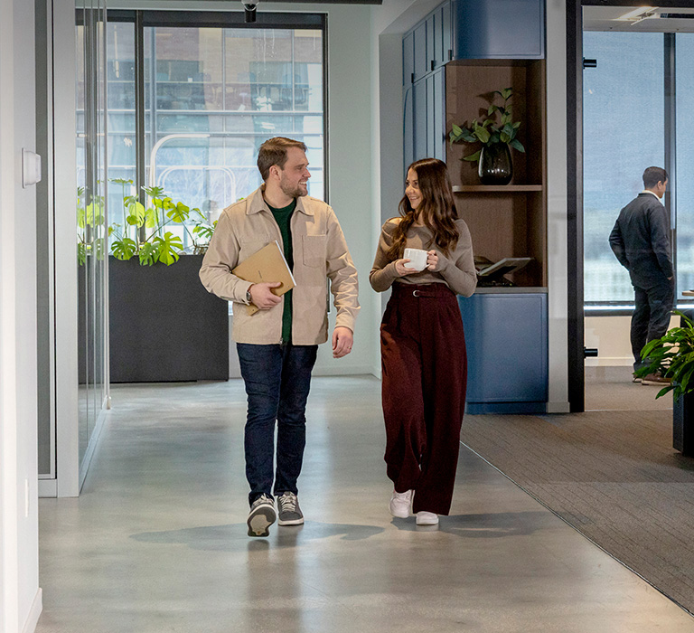 Image of two people walking down a hallway talking casually in an office building