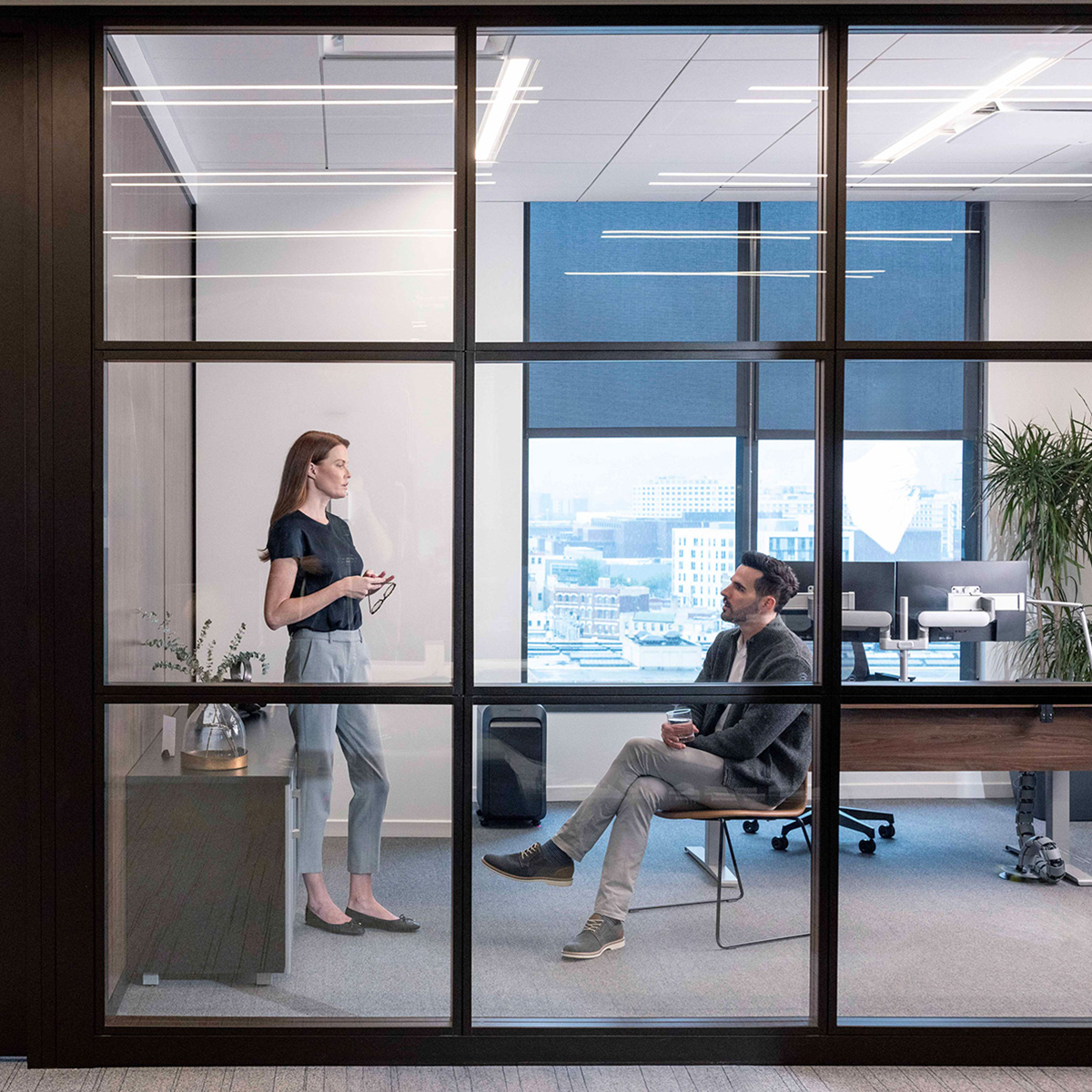 woman talking to sitting man in an office seen through glass wall